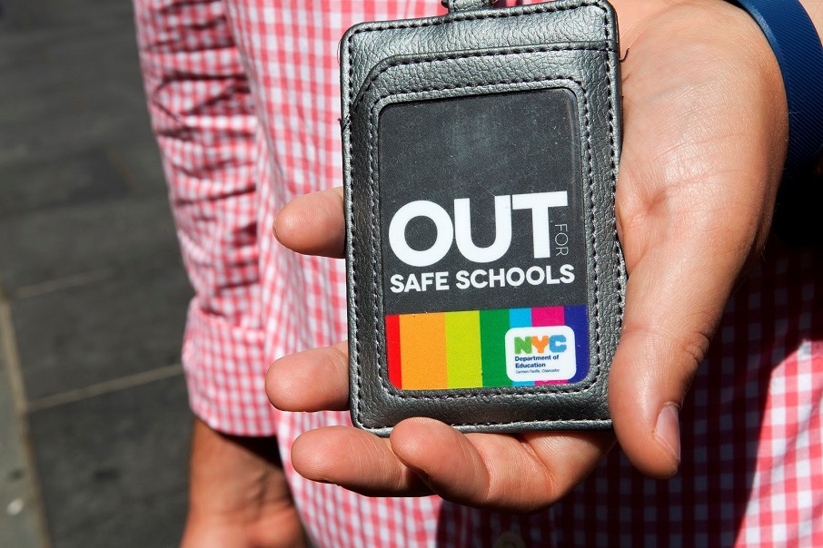 A person holds out a wallet showing an ID card that reads "Out for Safe Schools"