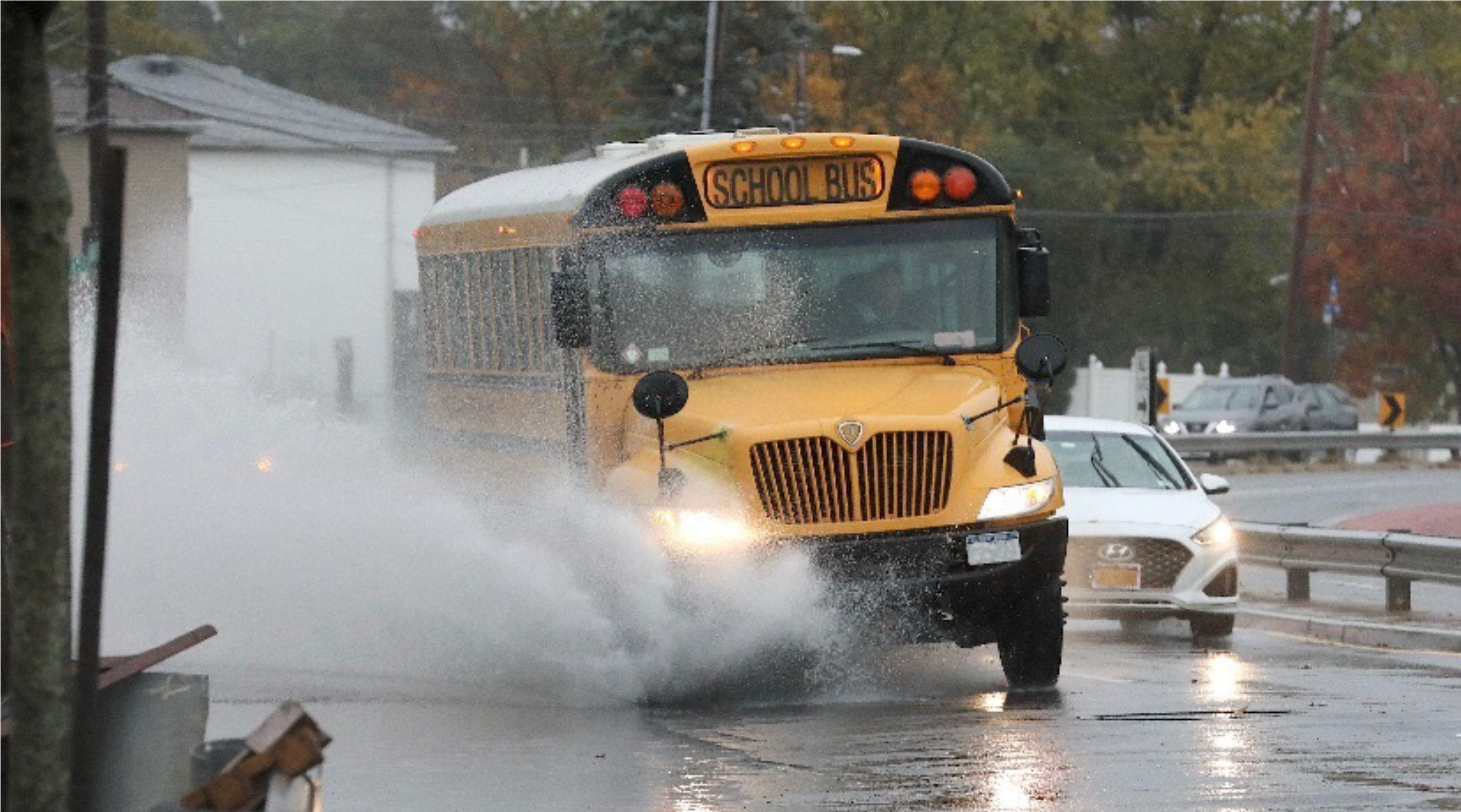 School Bus driving in the rain past a large puddle