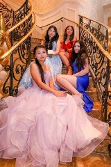 Four young women in formal prom attire sitting down on gold-rimmed stairway.