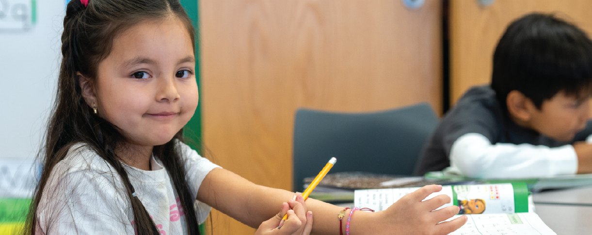 Young girl holding a pencil smiling in class