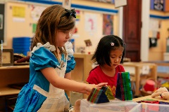 Two students dressed a fairy tale character and superhero playing with magnet tiles.