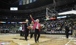 Woman wearing pink coat and walking across court while waving at crowd.