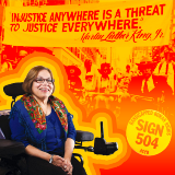 Photo of Judy Heumann in front of a sign reading "Injustice anywhere is a threat to justice everywhere."
