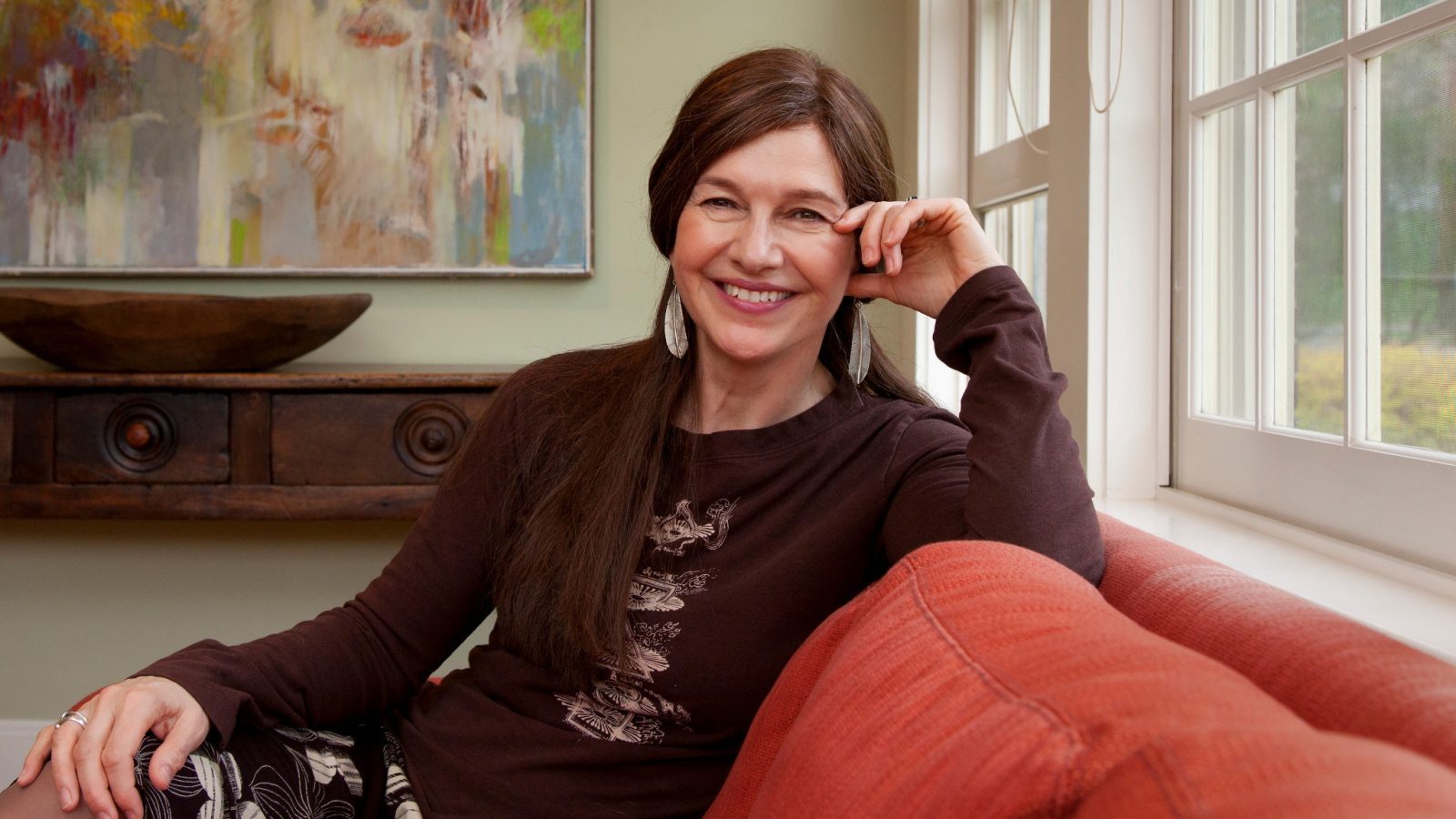 Pulitzer Prize winning author, Louise Erdrich, sitting on a red sofa