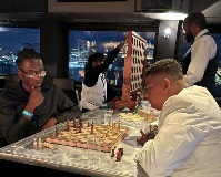 Two young men playing chess while in the middle of a formal gathering inside of a boat.