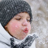 Close-up of child blowing snow into the air