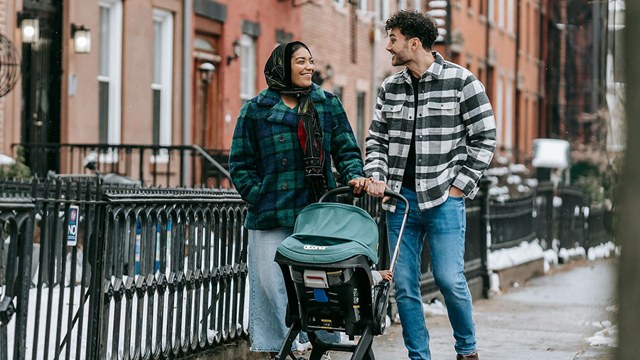Young couple happily walking down a street together while pushing a stroller.