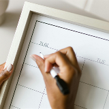 Close-up of a hand writing on a dry-erase calendar using a dry-erase marker.