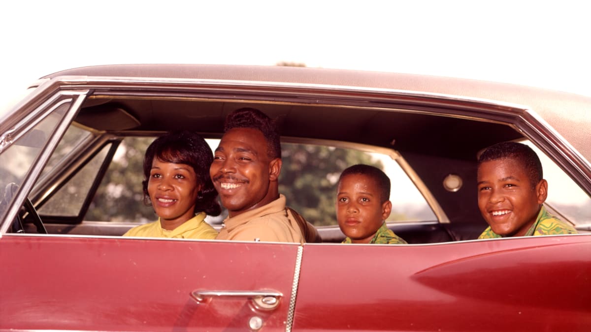 A family of four sitting inside of a 1950s-era vehicle and smiling