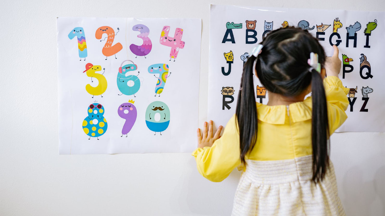 Girl in yellow dress reading English alphabet on wall