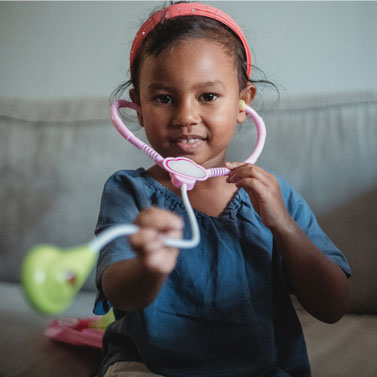 Young girl holding up a toy stethoscope to the viewer, as if ready to listen to a heartbeat.