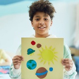 Student holding up paper art of the solar system.