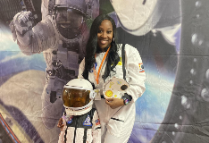 A student and teacher both dressed as astronauts pose in front of an outer space backdrop.
