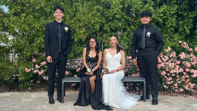 Two prom couples, posing around a garden bench. Two young men are flanking two seated young women.