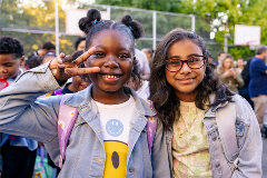 Two middle school-aged girls smiling and holding a "peace" sign with their hands.