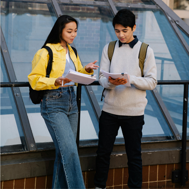 Two students having a conversation outside near a building skylight.