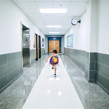 Single young student running down an empty school hallway heading towards the exit.